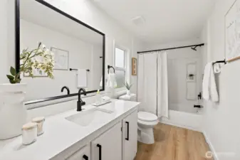 Stylish en suite bath with quartz countertop, white shaker vanity, black hardware, large framed mirror, and a tub/shower combo with a rain showerhead.