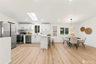 Updated kitchen with white shaker cabinetry, stainless appliances, quartz countertops, a skylight, and peninsula seating, open to the adjacent dining area.