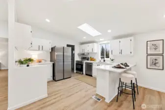 Well-appointed kitchen with white shaker cabinets, quartz countertops, stainless appliances, a skylight, and a peninsula with bar seating.