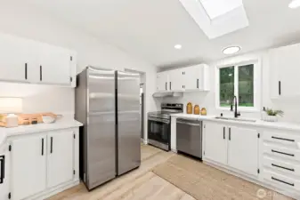 Clean, updated kitchen featuring white shaker cabinets with black hardware, stainless appliances, quartz countertops, skylight, and a window above the sink.