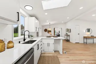 Kitchen view highlights the quartz sink, black gooseneck faucet, open sightlines through the dining and living areas, and abundant natural light from the skylight.