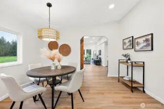 Bright dining area with a rattan pendant light, large window with green pastoral views, and open flow into the bonus living room beyond the arched doorway.