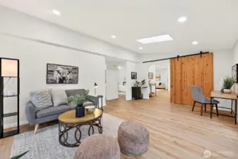 Generous bonus living room with a skylight, recessed lighting, LVP flooring, and a statement sliding barn door — open to bedrooms and the main living area.