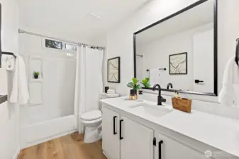 Updated full bath with white shaker vanity, quartz countertop, black hardware, large framed mirror, and a tub/shower combo with a built-in niche.