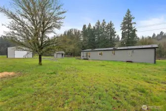 Rear view of the home with board-and-batten siding, multiple windows, sliding glass door access, and open green space with a detached garage and shed in the background.