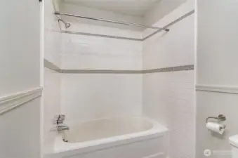 Another view of the bathroom, highlighting the tub and clean white tiling.