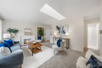The living room features a central skylight that adds natural brightness to the space. The fireplace is framed by a white brick-wrapped mantel that adds a clean, timeless touch. Neutral tones throughout the room create a calm backdrop for the built-in shelving and modern decor.