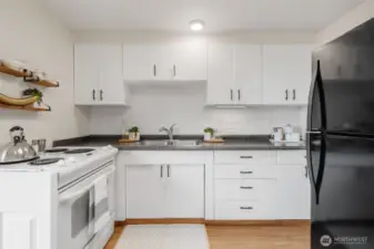 This kitchen features timeless white cabinetry paired with a durable laminate floor for easy maintenance and a clean look. A classic appliance package offers reliable functionality.