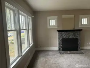 The wood-burning fireplace is the heart of this bright and beautiful living room and all its charm. wide baseboards and wood details remain from time gone by.