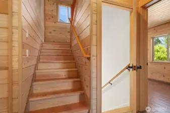Stairwell leading up to Primary and stairs leading down to storage & garage. One of 2 main level bedrooms to the right. All flooring is tile radiant heated - top of the line!