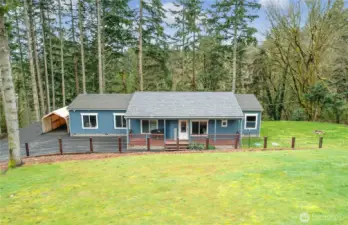 Private 1-level home on acreage with covered porch, lush lawn, and peaceful wooded backdrop.