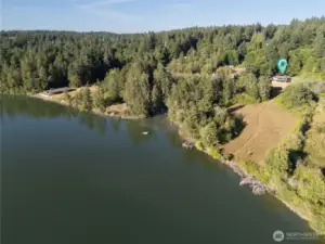 This aerial view captures the full scope of the property from beach to treetop. At low tide, the shoreline expands dramatically, showing off the reach of the 235 feet of waterfront on Henderson Inlet. The easement trail leads clearly back to the property and home, which is tucked into trees and surrounded by protected land. It’s privacy with presence and nature in every direction.