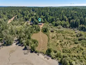 This aerial view captures the full scope of the property from beach to treetop. At low tide, the shoreline expands dramatically, showing off the reach of the 235 feet of waterfront on Henderson Inlet. The easement trail leads clearly back to the property and home, which is tucked into trees and surrounded by protected land. It’s privacy with presence and nature in every direction.