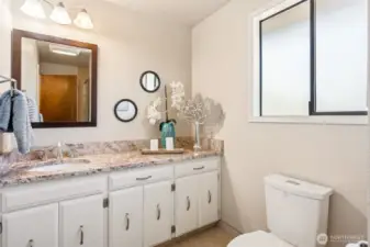 A large privacy-glass window adds light and ventilation without putting you on display. he long vanity counter gives you room to spread out, with crisp white cabinetry and an undermount sink that keeps the look clean and modern. A square, brown-framed mirror adds a little structure and contrast against the soft cream walls. The dual flush toilet keeps things eco-conscious without calling attention to itself.