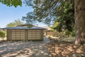 The two-car garage sits just off a wide, level driveway, with an easy, no-step transition to the walkway and front door. It’s a thoughtful layout that makes daily life simpler, especially when rain, leaves, or icy weather roll in. A tall evergreen shades the entry with soft, dappled light and brings a touch of natural drama to the front yard.