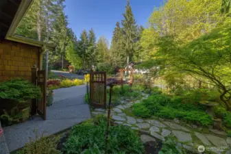 Looking from the front porch through the gate at the level parking area and all the flagstone pathways through the garden.