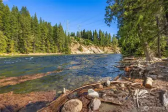 Peaceful Wenatchee River frontage with clear flowing water, natural shoreline, and a scenic backdrop of towering pines—offering a true mountain retreat setting.