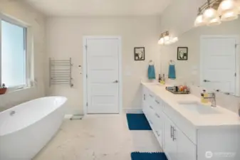 Double sinks, towel warmer, and door to the primary bedroom beyond.