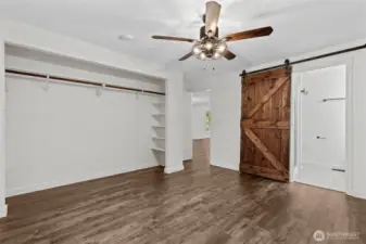 Open primary closet with built-ins and sliding barn-door to bath.