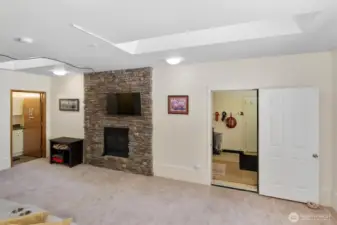 Lower-level living area with stone fireplace, carpet flooring, and doorway to storage or utility room.