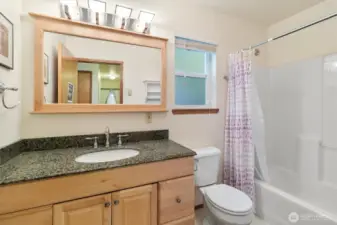 Bathroom between kitchen & primary bedroom with granite countertop vanity, framed mirror, and tub/shower combination.
