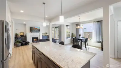 Bright and welcoming modern open-concept kitchen and living space featuring a granite island, stainless steel appliances, and cozy seating with natural light streaming through the curtains