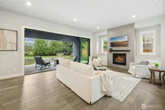 The light-filled living room features expansive sliding glass doors that create seamless indoor-outdoor flow to the private patio and landscaped backyard. A sleek tiled fireplace, clean architectural lines, and warm hardwood flooring anchor the space with modern elegance and everyday comfort.