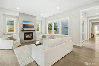 The open-concept living area is bathed in natural light from oversized windows, highlighting the home’s airy proportions and refined finishes. A contemporary gas fireplace with sleek tile surround creates a warm focal point, perfect for gathering or relaxed evenings at home.