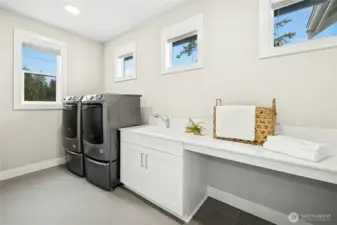 Conveniently located at the top of the stairs, the spacious laundry room features full-size appliances, abundant counter space, and built-in cabinetry for organized storage. A utility sink and dedicated folding area enhance everyday functionality while maintaining the home’s clean, modern aesthetic.