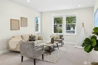 A closer view of the upper-level bonus room highlights its comfortable layout and flexible design, ideal for a media space, playroom, or home office. Large windows invite natural light while maintaining a bright, welcoming atmosphere throughout this versatile retreat.