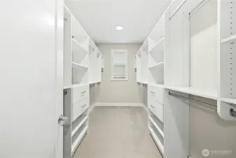 The spacious primary walk-in closet is thoughtfully designed with custom built-in shelving, hanging space, and drawer storage on both sides. A window at the end of the closet brings in natural light, creating a bright and functional dressing space with exceptional organization.