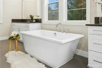 A closer view of the freestanding soaking tub highlights the spa-like atmosphere of the primary bath. Positioned beneath large windows, the tub is complemented by modern fixtures and nearby dual vanities, creating a tranquil space designed for relaxation and everyday comfort.