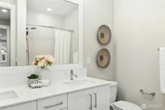 The upstairs shared bath offers a clean, modern design with a quartz-topped vanity, under-mount sink, and sleek chrome fixtures. A full tub and shower combination with tiled surround provides both style and everyday functionality. Neutral tones, ample mirror space, and quality finishes create a bright, polished space that comfortably serves the secondary bedrooms.