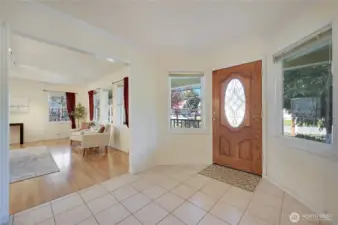 Welcoming tiled entry with decorative wood door, coat closet, and easy flow into the main living room—windows capture front-porch and neighborhood views.