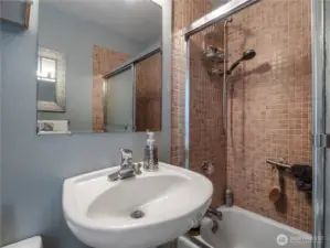 The bathroom saves space with a pedestal sink and features a beautiful tiled shower.