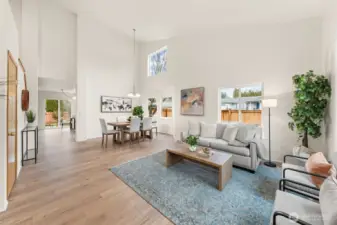 Soaring ceilings and laminate wide-plank flooring create a bright, open living space with seamless flow into the dining area. Large windows and a sliding door connect the interior to the backyard, enhancing everyday living and entertaining.