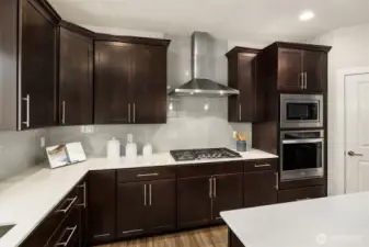 Closer view of cooktop, overhead vent, built-in microwave and oven.