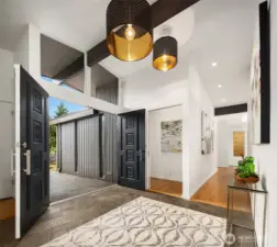 Original slate graces the front entry, with stunning original carved double entry doors offering privacy, while large/vaulted clerestory windows deliver soft light.     The doorway on the left leads to the primary suite, and the hallway takes you to kitchen/dining/family, and circles around to the living room which is directly behind us.  Off to the left are two large bedrooms, full bath, and stairs to the lower level.  For now let's pivot 180 degrees and head into the living room...