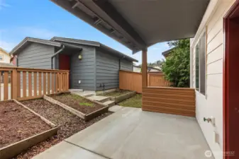 Covered back patio, fenced yard, planting beds, secure garage beyond.