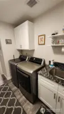 Utility room has a utility sink and added cabinets and shelving besides large washer and dryer.