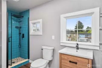 This modern bathroom combines eye-catching design with functional updates. A striking teal tile shower with black matte fixtures adds personality, while the large window and light wall tones keep the space feeling airy and bright. The sleek wood vanity brings warmth and style—proving that small spaces can still make a big impression.
