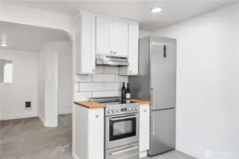 This well-appointed kitchen makes the most of its footprint with a modern stainless steel range, sleek vent hood, and matching fridge—all set against a backdrop of crisp white cabinetry and striking tilework. A touch of butcher block warmth frames the cooking space, blending efficiency and style in perfect balance. Ideal for any home chef or weekend cook who values both form and function.