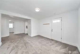 From this angle, you can see how the living area flows naturally into the kitchen and bedroom, making the most of its compact layout. Fresh carpeting and neutral tones make this space move-in ready and easy to personalize. The front entry adds convenience and charm.