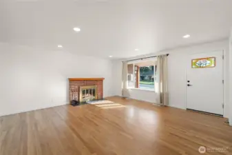 Bright and inviting living room featuring refinished original hardwood floors, a new mantle, updated lighting, a beautifully restored stained-glass front door and new energy-efficient windows throughout the home
