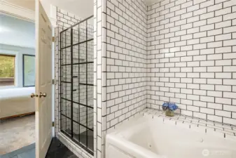 Beautiful primary bathroom tub and shower finished in white subway tiles with black accents.