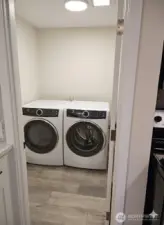 Dedicated laundry room conveniently located off the kitchen, featuring modern Electrolux front-load washer and dryer, bright lighting, and continuous waterproof laminate flooring throughout the home.