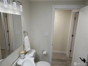 View from inside the bathroom toward the hallway. The bright lighting and clean trim highlight the smooth transition between the freshly updated bathroom and the rest of the home. The modern vanity, mirror lighting, and new waterproof laminate flooring tie seamlessly into the home’s contemporary interior style.
