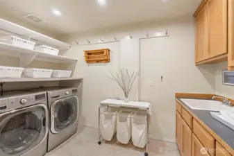 This spacious laundry room is thoughtfully designed with upper and lower cabinetry, open shelving, and a utility sink offering plenty of storage and workspace for laundry, cleaning supplies, or household organization.