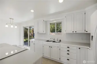Bright kitchen with white cabinets, storage, and slider to backyard.