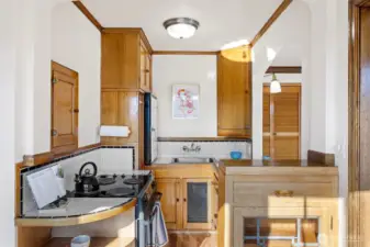 The kitchen is a charming blend of vintage character and function, featuring a built-in hutch with an original leaded-glass window, classic tile countertops and backsplash, and beautifully preserved glowing wood cabinetry. Thoughtful details like an old-fashioned icebox add to its timeless appeal.